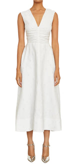 The person is wearing the exquisite Eliza Dress, a white Italian silk blend midi from Brandon Maxwell featuring a V-neck and bodice ruching, beautifully complemented by metallic pointed heels.