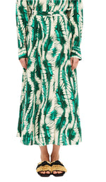A person is wearing a green and white patterned, long-sleeved dress made of 100% silk with a matching belt. They stand with arms at their sides. Black sandals featuring gold decoration are visible on their feet. The ensemble does not feature the Rowan Skirt by Ulla Johnson.