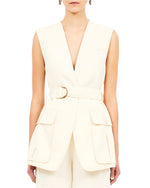 Someone is wearing the Ulla Johnson Twyla Vest, a sleeveless cream Tencel piece featuring a deep V-neck and large front pockets.