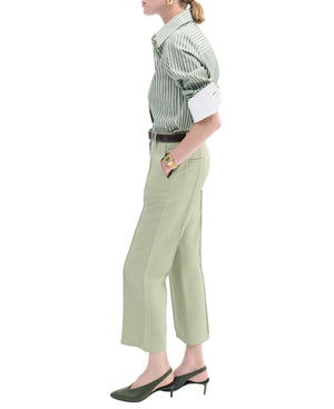A person in a CO Fitted Classic Shirt in green cotton poplin with stripes, paired with light green tailored cropped pants, green slingback heels, and gold jewelry, stands in side profile.