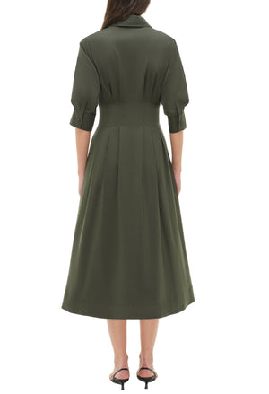 A woman stands facing away, wearing the Simkhai Signature Jazz Dress with three-quarter sleeves and black heeled sandals.