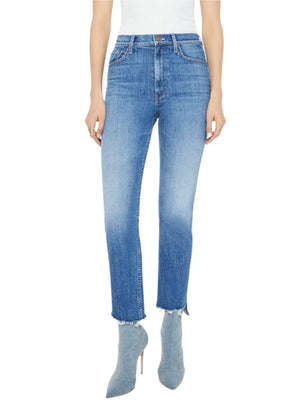 A person stands against a plain background, wearing High Waisted Rider Ankle Step Fray jeans by Mother in a mid-blue wash, paired with a white top and boots.