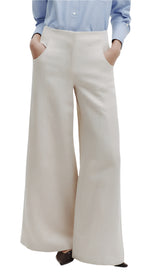 A person stands against a white background wearing the TWP Demie Linen Cotton Pant, a pair of high-rise beige wide-legged pants with hands resting casually in the pockets of the comfy twill.