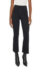 Model wears The Hustler Ankle Fray high-waist flare jeans by Mother in stretch denim with a raw hem, paired with a white top and black pointed-toe boots, shown from shoulders to feet against a white background.