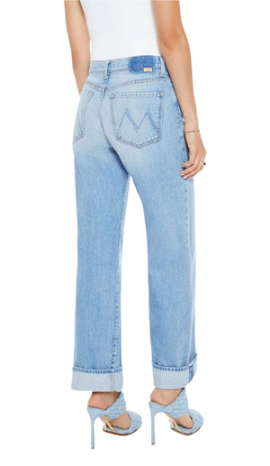 Someone wearing Mother’s Dodger Button Hover Cuff jeans in mid-blue with cuffed hems, a white top, and blue high-heeled sandals, seen from the back.
