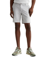 A person achieves a tailored look in light gray AG Jeans Wanderer Shorts, a white shirt, and green New Balance sneakers while standing against a plain background.