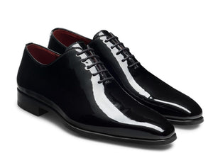 The Magnanni Cruz II Tux Shoes are black patent leather oxfords featuring closed lacing, low heels, and a slightly pointed toe, designed for formal wear with an elegant silhouette.