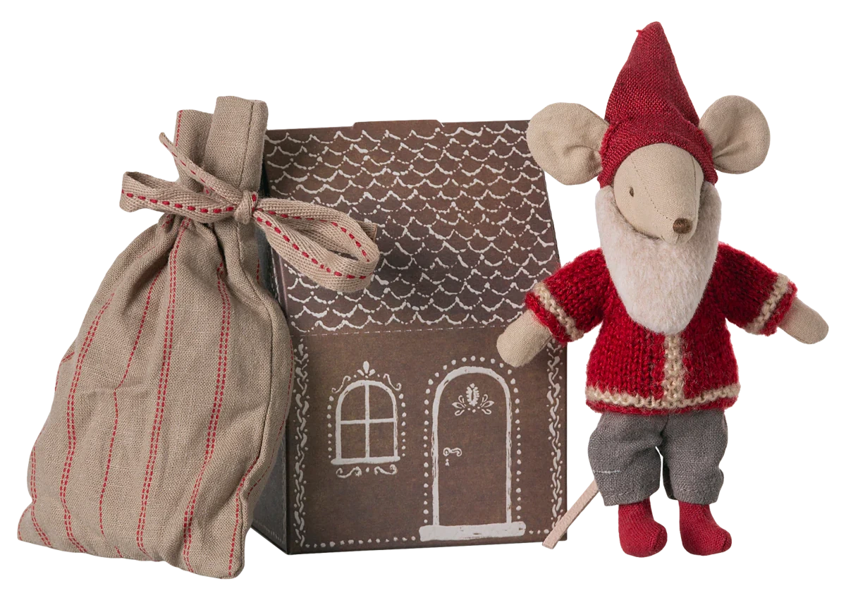 The Maileg Santa Mouse wears a red outfit and hat, standing beside a striped cloth bag and a cardboard Mouse Gingerbread House featuring white door and window designs.