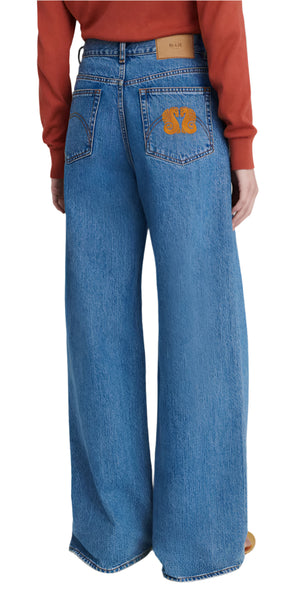 Wearing Blaze Milano's Nariida Java Jeans in classic blue with vibrant orange embroidery on the back pocket, paired with a striking red sweatshirt.
