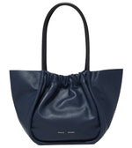 Proenza Schouler's Large Ruched Tote in navy blue leather showcases a ruched top, dual black handles, and a subtle logo stamp on the front, adding elegance to this stylish accessory.