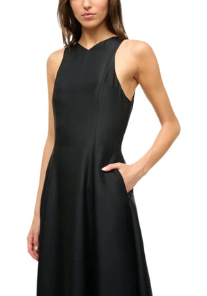 A woman models the Staud Heike Dress—a sleeveless, fitted black cocktail dress with a high neckline and side pocket—against a plain white background, making it an ideal choice for your next special event.