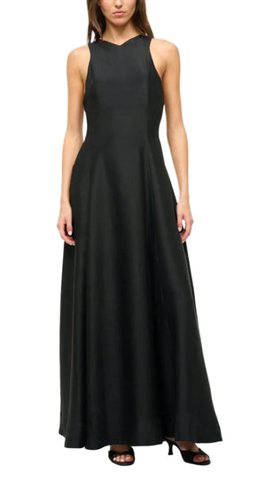 Perfect for special occasions, the Staud Heike Dress is a sleeveless, floor-length black maxi with a fitted bodice and flared skirt, styled here with open-toe black heels.