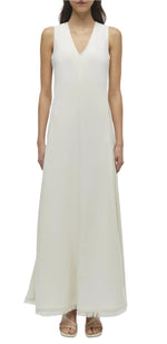 Front view of a woman wearing the Simkhai Lowri Dress, a sleeveless, white, floor-length dress with a fluid silhouette and V-neckline, paired with sandals.