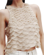 A woman in TWP's Shell Silk Organza Fishscales Top—a beige, elegant sleeveless crop crafted from silk organza with hand-sewn scallops—styled chicly with white pants.