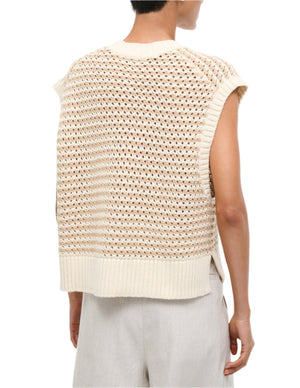 Model wearing the Staud Americana Sweater, a cream-colored, sleeveless chunky knit vest with a textured pattern and cropped fit, shown from the back and styled with light-colored pants.