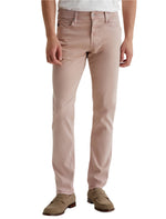 A man wears AG Jeans' Tellis Modern Slim Sueded Stretch Sateen light pink pants with five pockets, perfectly paired with a white shirt and brown suede loafers.