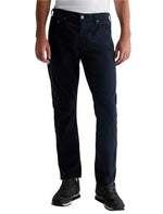 A person wearing AG Jeans' Everett Sueded Slim Straight jeans with a mid-rise waist and black sneakers, standing against a white background.