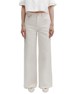 A person wears TWP Tiny Dancer Jeans—high-waisted, vintage-inspired wide-leg denim—with a cropped white shirt and white shoes, standing against a plain white background.