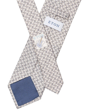 The Eton Off White Geometric Link Tie exudes classic elegance and showcases sartorial flair with its geometric design, blue polka dot lining, and guitar motif label.