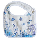 The Perfect Bib by Timo & Violet: a white muslin bib with blue ocean-themed illustrations of fish, coral, and waves, secured with a metal snap button.