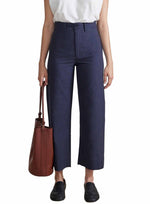 Someone is sporting Apiece Apart's Classic Merida dark blue high-waisted wide-leg pants, paired with a white sleeveless top and black shoes, while carrying a brown leather handbag.