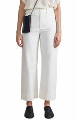 Person wearing Apiece Apart's Classic Merida Pant in white, paired with a white top, black loafers, and carrying a small black crossbody bag.