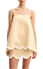 A woman wears the Essie Top by POSSE, a sleeveless cream linen piece featuring a square neckline and delicate scalloped hem.