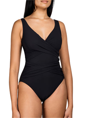 A woman wears the Karla Colletto Smart Surplice One Piece, a black, sleeveless V-neck swimsuit with a wrap-style waist that flatters and highlights her silhouette.