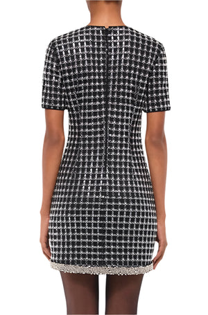 Someone wearing the Simkhai Vivalie Mini Dress—a short-sleeve, black and white checkered style with a beaded hem—shows off its relaxed fit and flattering silhouette from the back.