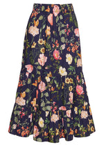 The Chase Skirt by Cara Cara is a dark blue cotton poplin midi skirt with colorful floral and leaf prints, an elastic waistband, and tiered design.