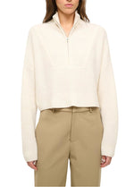A person wearing a cream Cropped Hampton Cashmere Sweater by Staud with beige high-waisted trousers, waist up against a white background.