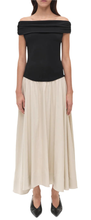 A woman wears the Simkhai Adaline Off Shoulder Midi Dress, featuring a sculpted bodice in black, styled with black pointed-toe shoes.