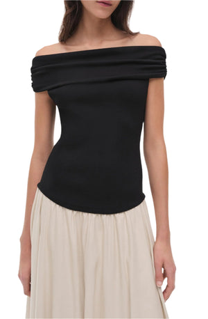 A woman models the Simkhai Adaline Off Shoulder Midi Dress, showcasing a fitted bodice and black off-the-shoulder top with a flowing skirt, captured from shoulders to hips against a plain backdrop.