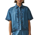 A person wearing the Carolina K Pina Shirt, a short-sleeve Tencel denim blue shirt with spread collar and swirl embroidery, paired with matching blue bottoms.