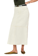 A person wearing The Flounce Denim Skirt by Frame, a cream-colored maxi with front pockets, styled with a black belt and brown flat shoes. Upper body is not visible.