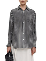 A person wearing an Oversized Tunic Shirt by Maria McManus, featuring a black and white striped pattern, and white pants holds a black woven bag, evoking a vintage-inspired style.