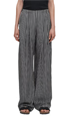 A person stands against a plain background, wearing the Maria McManus Flap Pocket Pleat Pant in black and white stripes, with a vintage-inspired wide-leg silhouette, paired with sandals.