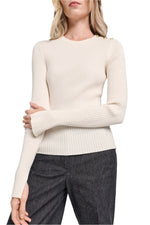 Wearing the Dorothee Schumacher Essential Ease Pullover, a cream ribbed wool-silk blend sweater with a round neck, and dark gray pants, the person stands with arms loosely crossed.