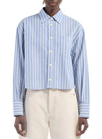 A person is seen wearing the Cropped Oversized Shirt by Maria McManus, a blue and white vintage stripe design with long sleeves and a pocket, crafted from organic cotton, perfectly paired with light-colored pants.