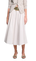 A person stands against a white background wearing Dorothee Schumacher's Poplin Power Skirt, styled with a light beige cardigan, wide belt, and green open-toe sandals.