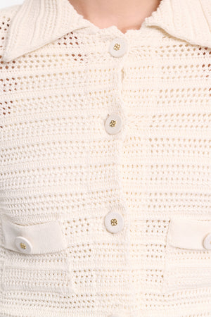 Close-up of the Dorothee Schumacher Precise Pointelle Jacket—a cream-colored, crocheted shirt with a graphic pointelle pattern, four buttons, and two chest pockets, worn by a person.