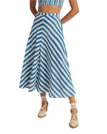 A person wearing a blue and white handloom cotton crop top with the Marta Ikat Stripe Skirt by Emporio Sirenuse, paired with beige espadrilles, stands elegantly against a pristine white background.