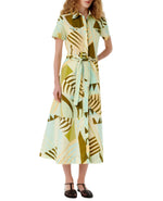 A person wears the Emporio Sirenuse Giselle Pagoda Dress, a short-sleeved chemisier with Bali-inspired geometric green, yellow, and blue designs. Black shoes complete the look against a plain white backdrop.