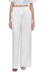 Person wearing Simkhai Olly Double Waistband Pants, featuring high-waisted, wide-leg design, paired with a cropped white top and open-toe shoes.