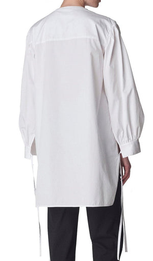 A person is seen from the back, wearing the CO Cuff Tie Shirt, a loose-fitting blouse with strings and wide sleeves that billow gently.