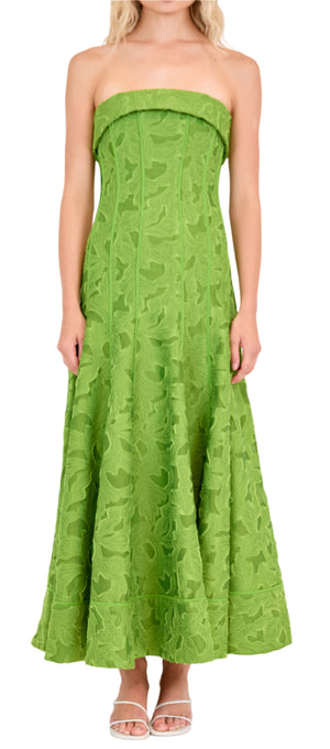 A woman wears the Simkhai Imogen Midi Dress, a strapless green Summer Jacquard style in Kiwi with a floral textured pattern, paired with white open-toe sandals.