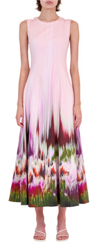 A person wearing the Simkhai Magnolia Midi Dress, a sleeveless dress with an abstract print on the lower half, paired with white heeled sandals.