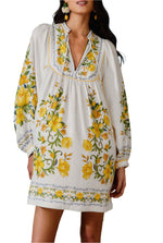 A woman wears the Farm Rio Sicily Scarf Off White Mini Dress, a long-sleeve white mini dress with yellow floral embroidery, standing against a plain background.