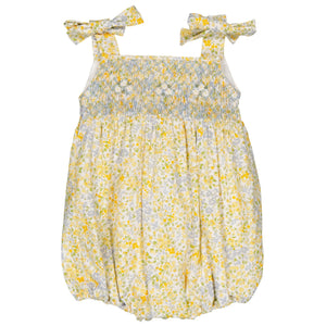 The Kidiwi Baby Girls' Francine Smocked Romper showcases a charming floral print in yellow and blue, with a hand-smocked neckline and bow-tie shoulder straps.