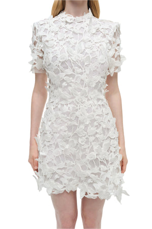 A woman wears the Simkhai Darla Mini Dress, a short-sleeve white lace dress with intricate 3D floral guipure appliqué for a refined statement look.